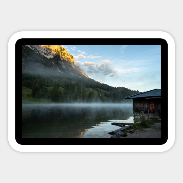 Misty Lake Portrait wide angle with boathouse. Amazing shot of a wooden house in the Ferchensee lake in Bavaria, Germany, in front of a mountain belonging to the Alps. Scenic foggy morning scenery at sunrise. Sticker by EviRadauscher